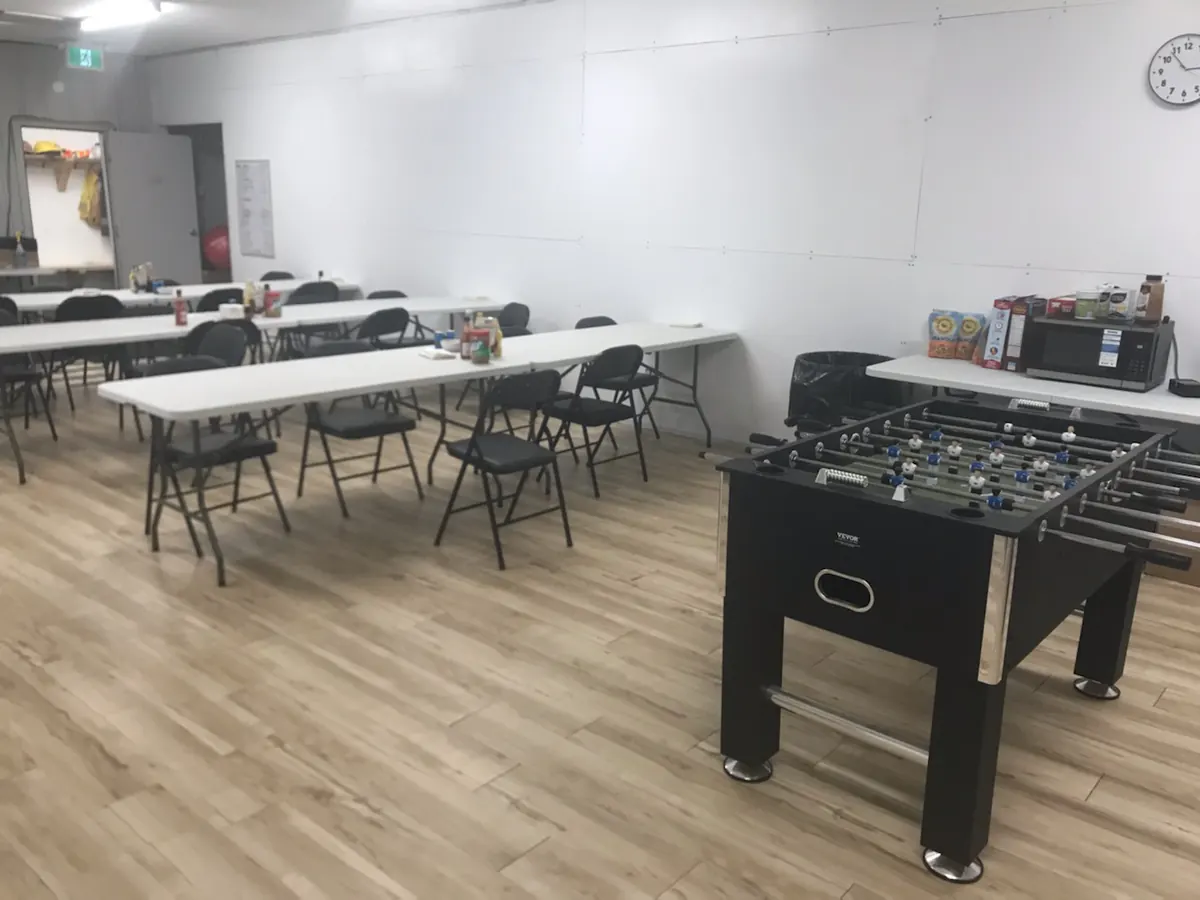 A bright camp dining room with long tables, folding chairs and a foosball table