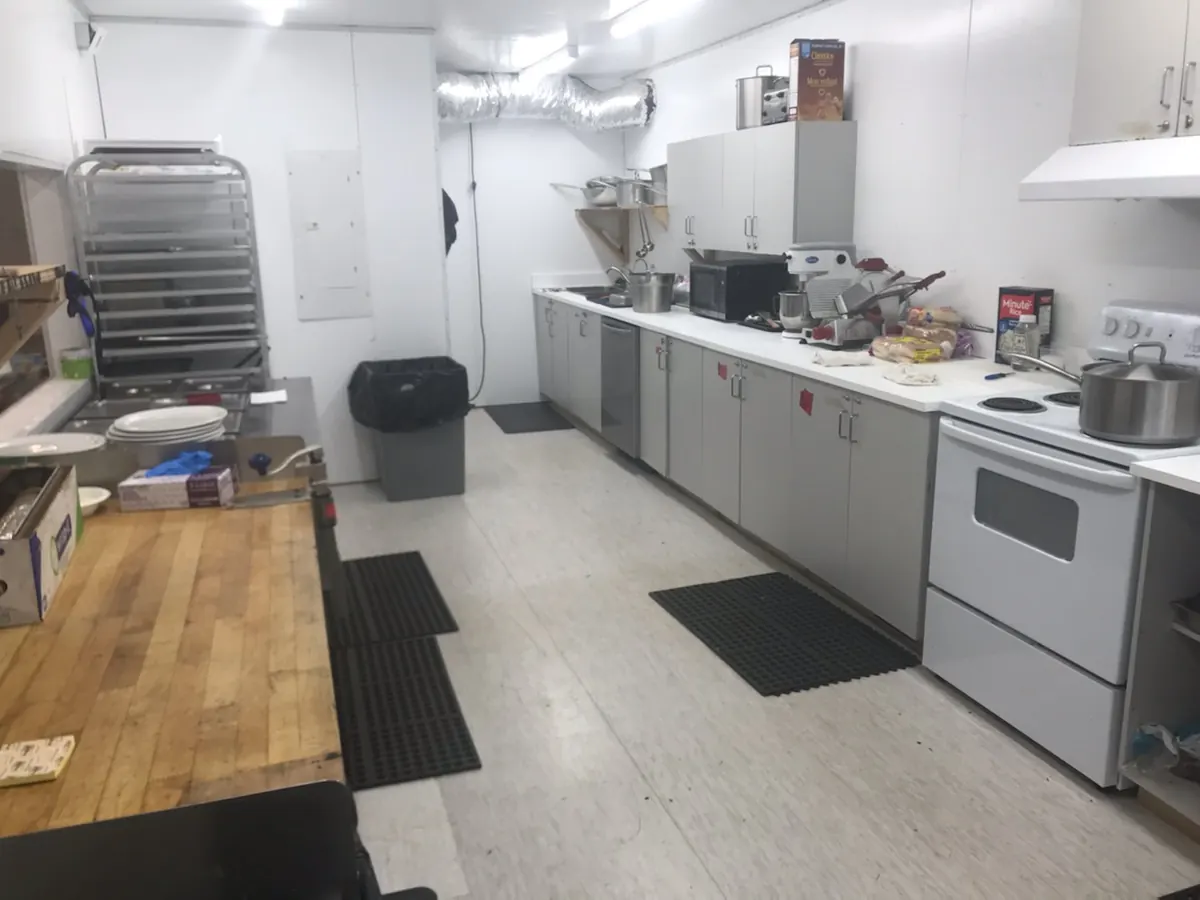 A clean camp kitchen with a butcher-block counter, stoves and a sheet-pan rack