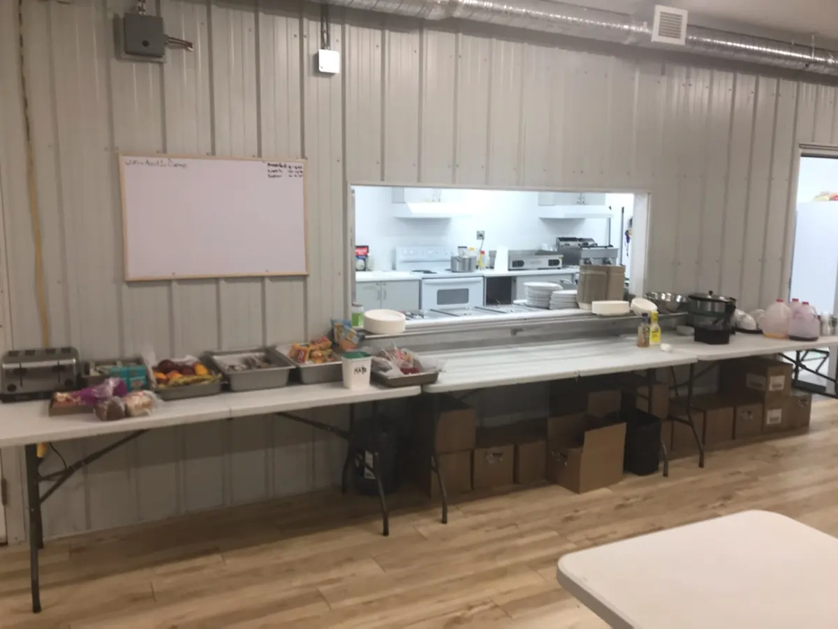 A camp servery with trays of food laid out on a long table in front of the kitchen window